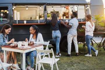 Multiracial people eating at gourmet meal at food truck restaurant outdoor - Healthy meal and summer dinner concept - Focus on african woman face