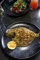 fried flounder with onion and lemon on a black clay plate