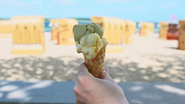 Slow motion 4K video of hand holding ice cream in waffle on a Baltic sea beach at summer day