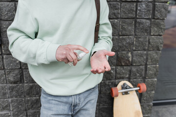 cropped view of man applying sanitizer on hand near blurred longboard.