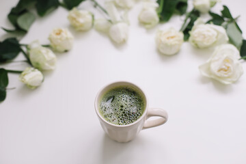 A cup of matcha tea and roses on white background. Flatlay, top view