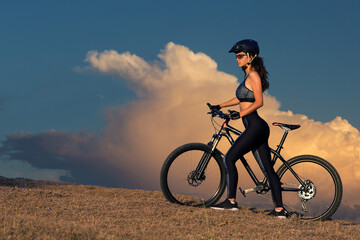 Girl on a mountain bike on offroad, beautiful portrait of a cyclist at sunset, Fitness girl rides a modern carbon fiber mountain bike in sportswear.