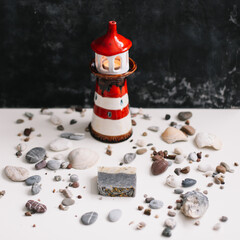 A small decorative lighthouse with sea shells and pebbles. Summer, holidays and vacation concept