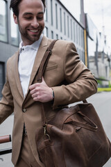 happy businessman in suit holding leather bag and smiling outside.