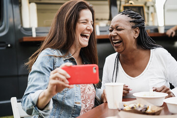 Multiracial women having fun taking photos with mobile phones at food truck restaurant outdoor - Summer, dinner and friendship concept - Focus on african american female face
