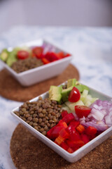 Lentil salad in square plates, with pieces of avocado, cherry tomato, onion.