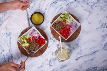 View from above of hands picking up the lentil salad with pieces of avocado, cherry tomato and...