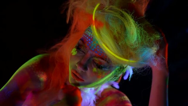 mysterious female character with fluorescent makeup on face, closeup portrait in darkness