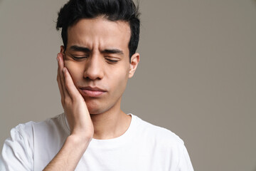 Brunette hispanic man with toothache frowning and rubbing his cheek