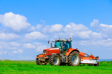 Large red tractor with a mower mows the grass on a field on a sunny day