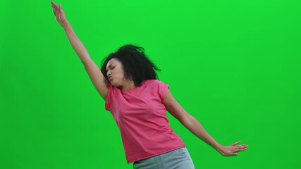 Portrait of young female African American cheerfully dancing the dance of victory, joy or good mood. Black woman with curly hair poses on green screen in studio. Close up. Slow motion ready 59.97fps.