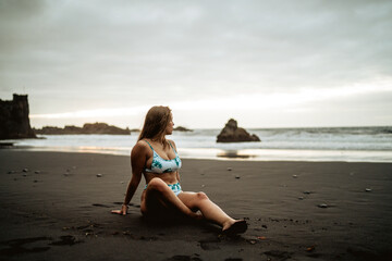 Fototapeta na wymiar Chica veraniega guapa en una playa de arena negra durante el atardecer luciendo su bikini de moda