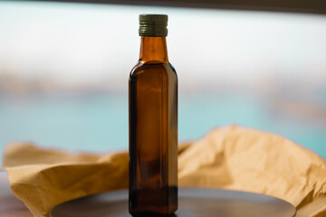 A glass brown transparent faceted bottle full of vegetable oil with green metal cap stands on plate on paper. Salad dressing. Linseed, olive, rapeseed oil. Blue background.