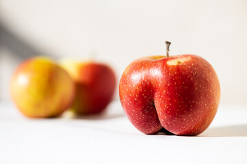 Bright ripe red apple of an unusual shape in the shape of an ass in the sunloght on a white...