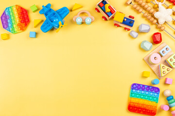 Baby kids toys background with wooden toys, abacus, plane, pop it fidget toys and colorful blocks on yellow background. Top view, flat lay