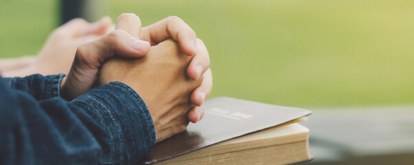 Hands folded praying over a Bible, hands over soft focus Bible.For banner.Holy Bible in church...