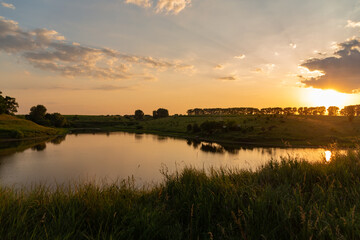 beautiful sunset on the lake in the middle of a field with trees in summer
