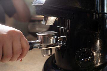 close-up of a barista holding a coffee portafilter. Electric coffee grinder in the coffee shop. The concept of the process of preparing beans for the preparation of aromatic espresso.