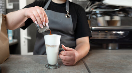 close-up of a barista woman preparing a latte pours coffee into a glass from a metal jug. The...