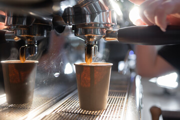 Close-up of a coffee machine making an espresso. The coffee flows into a paper cup under the metal spout of the coffee maker. Production of hot coffee.