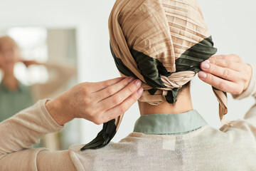 Back view at mature woman putting on headscarf by mirror and getting ready to go out, copy space - obrazy, fototapety, plakaty