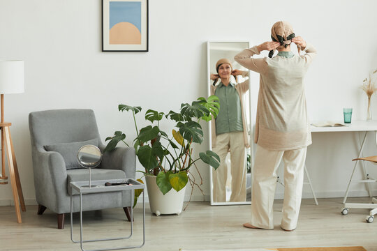 Full Length Back View At Mature Woman Putting On Headscarf While Looking At Mirror And Getting Ready To Go Out, Copy Space