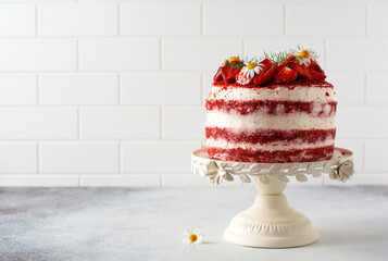 Red velvet cake with strawberry, whipped cream and bouquet of daisies on white board on gray...