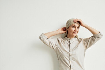 Minimal waist up portrait of smiling mature woman wearing headscarf and looking at camera while standing by white wall, copy space - obrazy, fototapety, plakaty