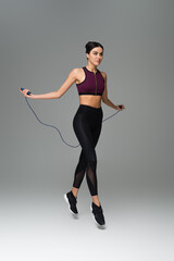 full length view of sportive woman training with jump rope on grey background. - obrazy, fototapety, plakaty