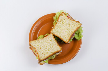 Sandwiches and brown clay plate on white background. Square sandwiches with ham, tomato, lettuce, dill, sauce.