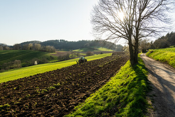 Im Märzen der Bauer, Landwirt mit Traktor und Pflug beim umpflügen des Ackerbodens in der Abendsonne.