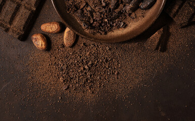 Chocolate and cacao concept. Cocoa powder in bowl near cocoa beans and broken chocolate on black...