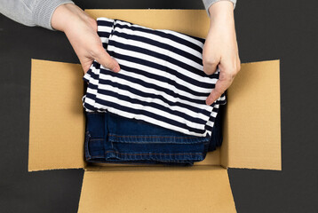 A woman puts clothes in a box - a striped T-shirt and jeans. Concept delivery, packaging