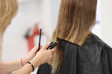 Hairdresser doing hair cutting of woman using clipper in salon closeup