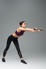 sportswoman doing forward bends with dumbbells on grey background.