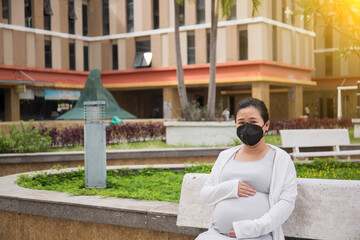 Portrait of pregnant  woman wearing masking sitting on a bench in the park 