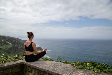 Fototapeta premium Woman doing yoga on the top of a mountain on a sunny day.Girl on a mountain striking a balance yoga pose feeling at peace with nature.Young woman doing yoga outdoors with amazing back view. Bali.
