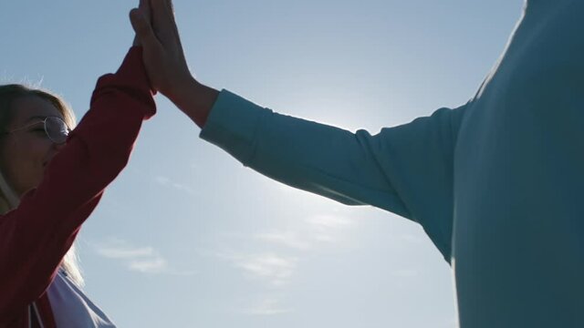 Amazed long haired blonde in red hoodie gives high five to guy at back bright sunlight under blue sky super slow motion closeup