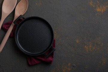 Empty cast iron pan on concrete background with wooden spoon and spatula with copy space. 