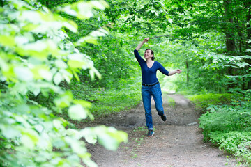 Naklejka na ściany i meble Happy middle-aged woman walks through the summer forest.