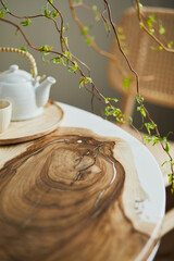 Interior design of stylish dining room interior with family wooden and epoxy table, rattan chairs, flowers in vase and teapot with cups.  Details. Template.