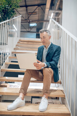 Man with laptop sitting on stairs in office