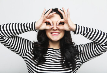 Cheerful brunette woman looks through zero or ok gesture, holds rounded fingers near eye