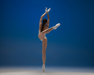 Back view. Young beautiful ballerina in action isolated over blue background. Concept of beauty,...