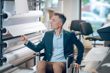 Man in wheelchair looking at paper rolls