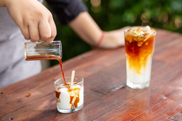 A small clear glass filled with white coconut ice cream and poured coffee. There is coconut water mixed with coconut meat in a clear glass next to it. Coffee drink design concept with fruit.