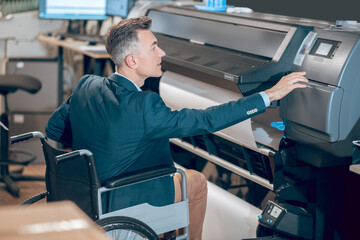 Profile of man in wheelchair touching copier