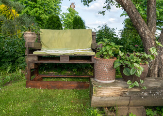 Fototapeta na wymiar the green garden in summer, homemade wooden chair from pallets for relaxing in the garden, blooming colorful flowers in pots