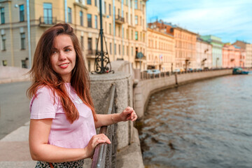 Fototapeta na wymiar A beautiful young woman walks through the city center along the canals on a summer day, a popular tourist destination of St. Petersburg