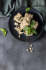 Pieces of halva on black plate. Sweet dessert with mint leaves on black background
